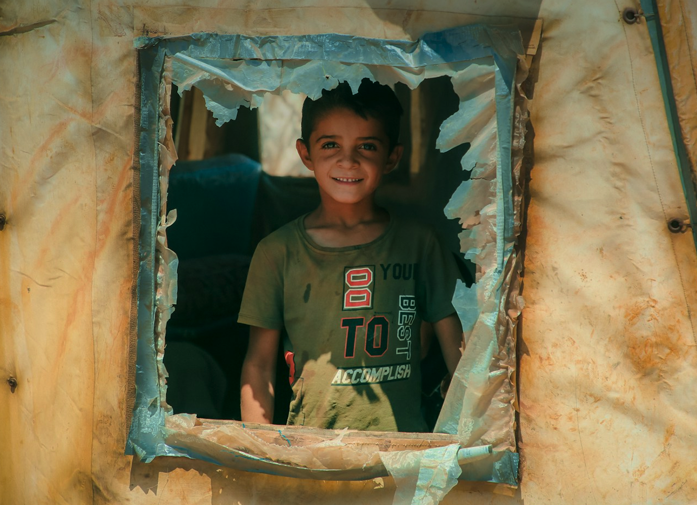 Niño sonriendo desde la ventana de una tienda de campaña.
